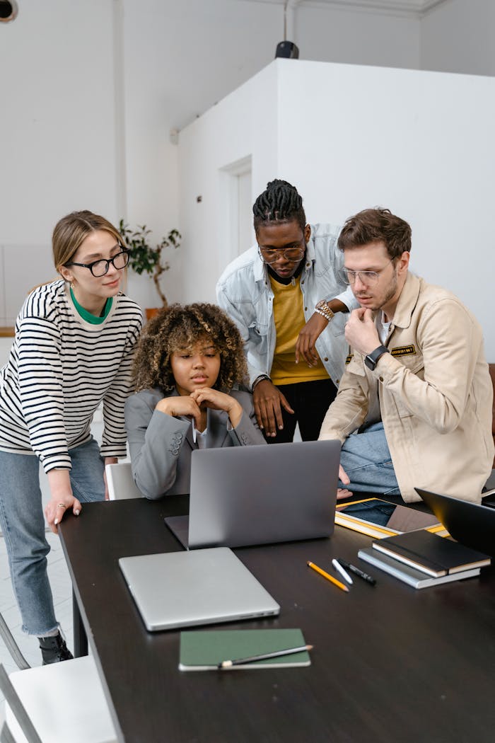 A diverse team of adults collaborating in a modern office setting with laptops and notebooks.